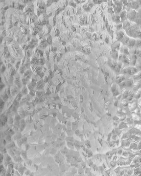 Close-up abstract texture of frosted glass block with translucent wavy patterns and distorted light, creating a soft architectural background.