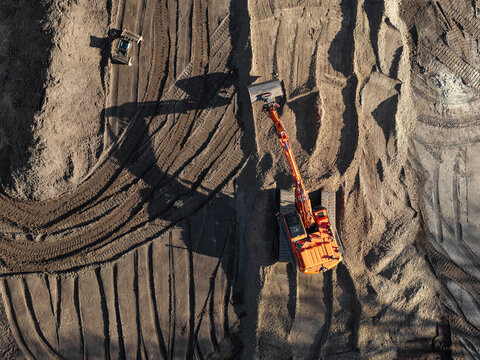 Aerial view of an orange excavator working on a construction site with deep tire tracks in the dirt in Enschede, Overijssel, Netherlands.