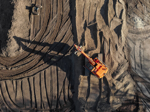 Aerial view of an orange excavator working on a large construction site with deep tire tracks in the soil in Enschede, Overijssel, Netherlands.
