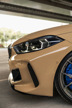 ew BMW 1 Series in a refined sand beige finish parked on asphalt beneath a modern city bridge highlighting compact proportions, sharp design, premium details and contemporary German automotive styling