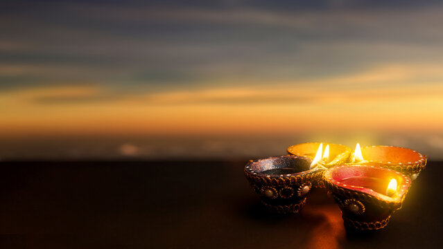 Lit decorative clay diya lamps glowing at sunset for Diwali celebration, featuring ample copy space. Diwali festival celebration