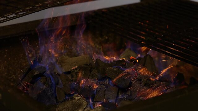 A fierce fire in an iron grill, closeup shot in the evening light, glowing coals and sparks flying in all directions, preparing the barbecue for grilling meat.
