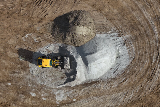 Aerial view of a yellow wheel loader working on a construction site with large piles of sand and gravel in Enschede, Overijssel, Netherlands.