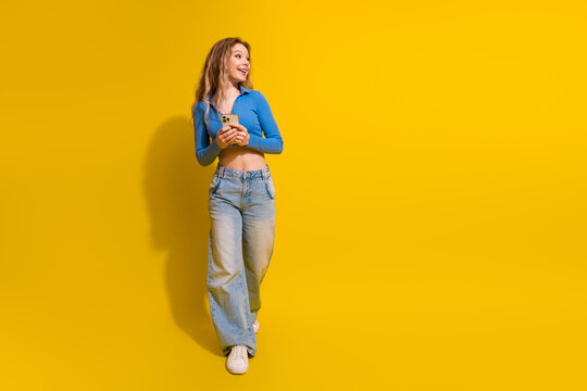 Happy young stylish woman holding smartphone in a vibrant yellow background indoor studio shot
