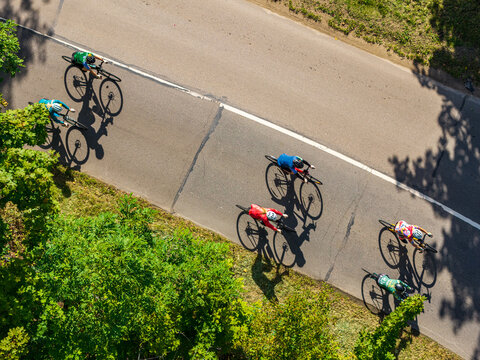 Aerial view of cyclists riding on an asphalt road, with long shadows cast on the pavement, surrounded by green trees in Vilnius, Vilnius County, Lithuania.