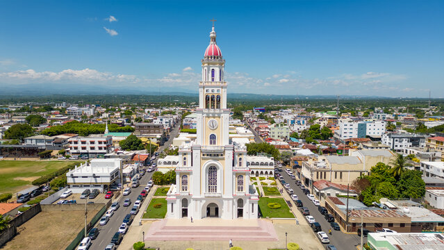Aerial view of the Iglesia Sagrado Corazon de Jesus, a church with a clock tower and red dome, surrounded by the urban landscape of Moca, Espaillat Province, Dominican Republic.