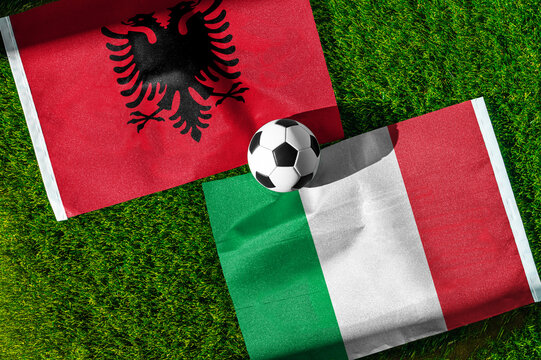 Albania vs. Italy football match. National flags on green grass with soccer ball in the middle. Football background for international match.