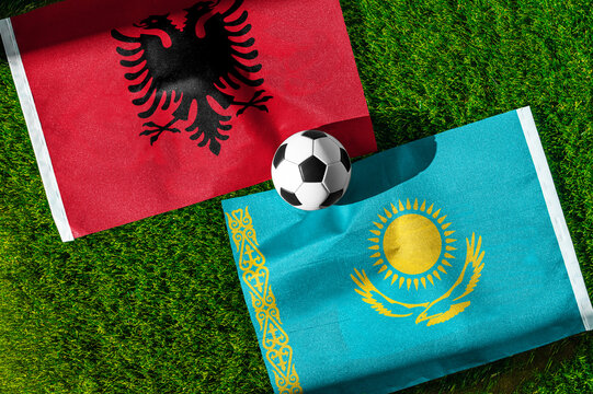 Albania vs. Kazakhstan football match. National flags on green grass with soccer ball in the middle. Football background for international match.