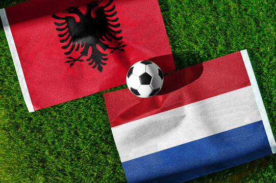 Albania vs. Netherlands football match. National flags on green grass with soccer ball in the middle. Football background for international match.