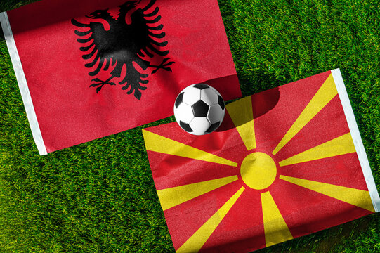 Albania vs. North Macedonia football match. National flags on green grass with soccer ball in the middle. Football background for international match.