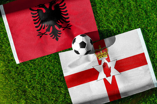Albania vs. Northern Ireland football match. National flags on green grass with soccer ball in the middle. Football background for international match.