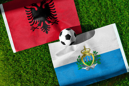 Albania vs. San Marino football match. National flags on green grass with soccer ball in the middle. Football background for international match.