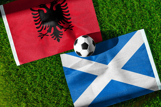 Albania vs. Scotland football match. National flags on green grass with soccer ball in the middle. Football background for international match.