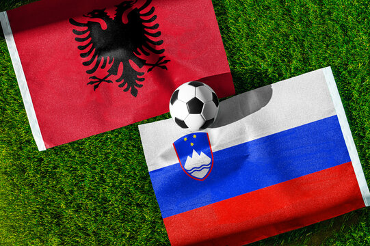 Albania vs. Slovenia football match. National flags on green grass with soccer ball in the middle. Football background for international match.