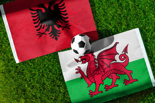 Albania vs. Wales football match. National flags on green grass with soccer ball in the middle. Football background for international match.