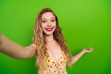 Obraz premium Smiling young woman with blonde hair in floral top posing for selfie against green background in casual fashion lifestyle shoot