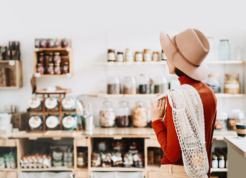 A caucasian female shopper stands with her back to the camera, looking at organic goods on wooden shelves inside a bright modern store interior.