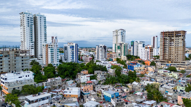 Aerial view of the urban landscape featuring high-rise towers, dense residential neighborhoods, and lush greenery under a cloudy sky in Santo Domingo, Distrito Nacional, Dominican Republic.