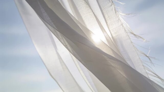 Billowing in light breeze white fabric shifting and revealing sun against clear sky, frayed edge