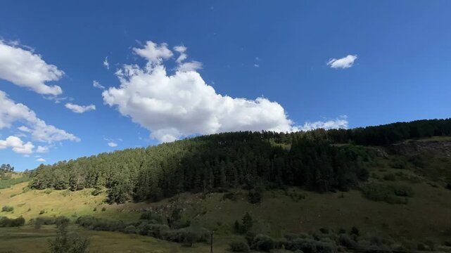 Cinematic time-lapse of fast-moving clouds over lush green hills and a bright blue sky in Sarıkamış, Anatolia