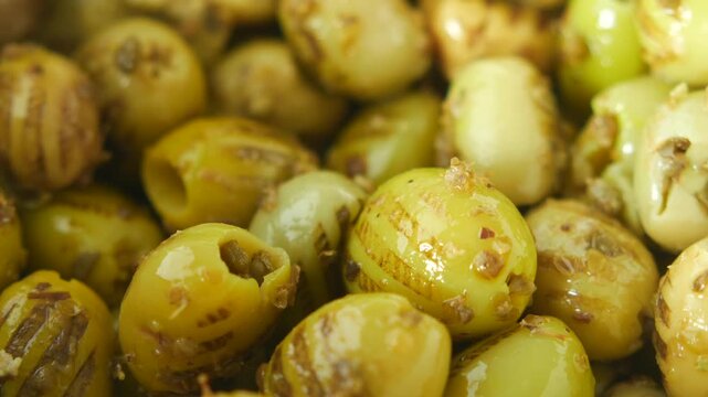 Grilled green olives with herbs in white bowl rotating slowly in macro shot