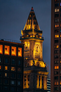 Aerial view of the illuminated Custom House Tower clock tower at night, surrounded by historic and modern architecture in Boston, Massachusetts, United States.