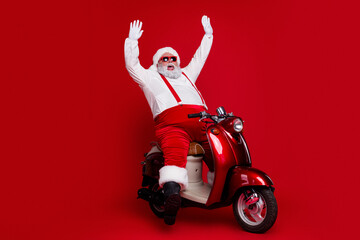Naklejka premium Santa Claus riding a red vintage scooter wearing sunglasses and waving joyfully on a bold red background for festive Christmas holiday fun