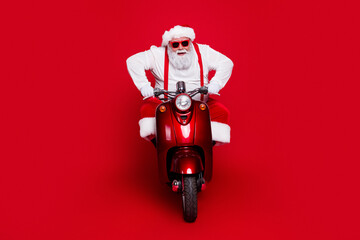 Naklejka premium Santa Claus riding a red scooter wearing sunglasses and a festive suit against a bold red background, playful modern Christmas concept and holiday spirit