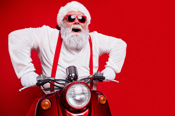 Naklejka premium Santa Claus in red sunglasses and suspenders riding a vintage red scooter with joyful expression for Christmas fun and holiday celebration