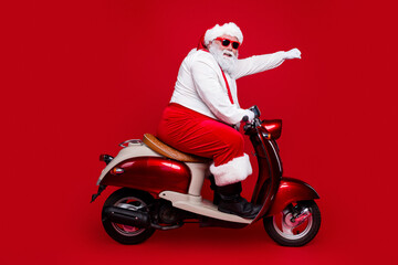 Naklejka premium Santa Claus riding a red scooter wearing sunglasses and a festive suit, waving on a bold red background