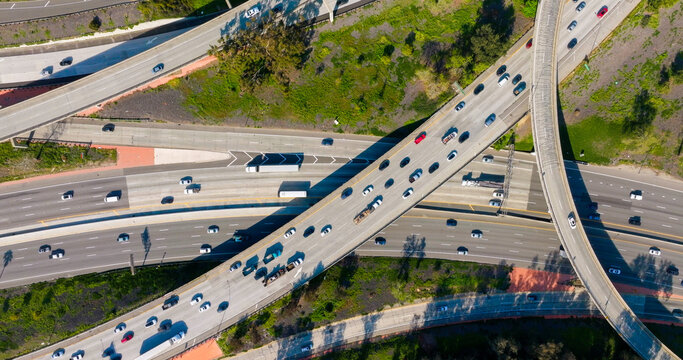Aerial view of a busy highway interchange with multiple lanes of traffic, trucks, and cars navigating the concrete roads surrounded by green vegetation in Los Angeles, California, United States.