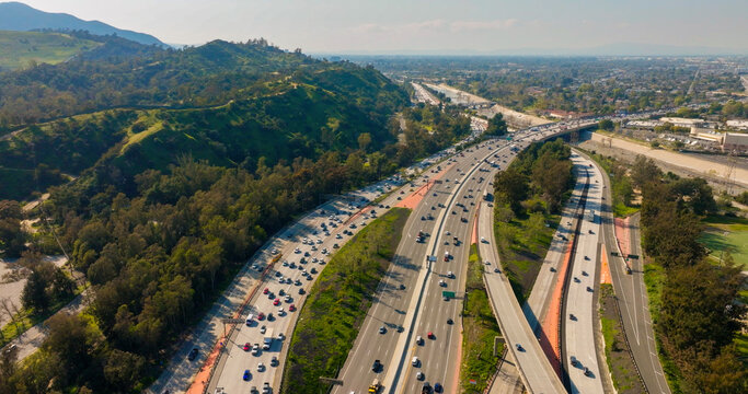 Aerial view of busy freeway with heavy traffic winding through green hills and urban landscape in Los Angeles, California, United States.