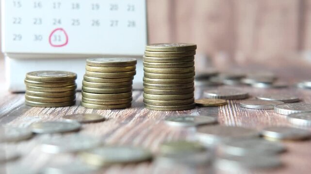 Stacking coins on wooden table with calendar and calculator showing financial growth and savings concept