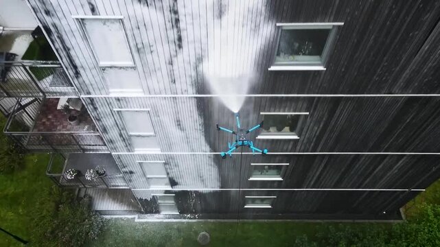 Innovative drone technology using a high pressure water jet to clean the dark wooden exterior of a multi story apartment building, showcasing an efficient and modern maintenance solution