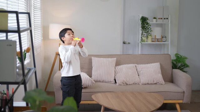 Happy asian boy playing toy trumpet and dancing with his sister at home in the living room