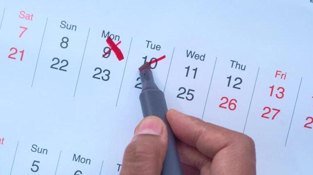 Close up hand crossing off dates on calendar with red marker for deadline management