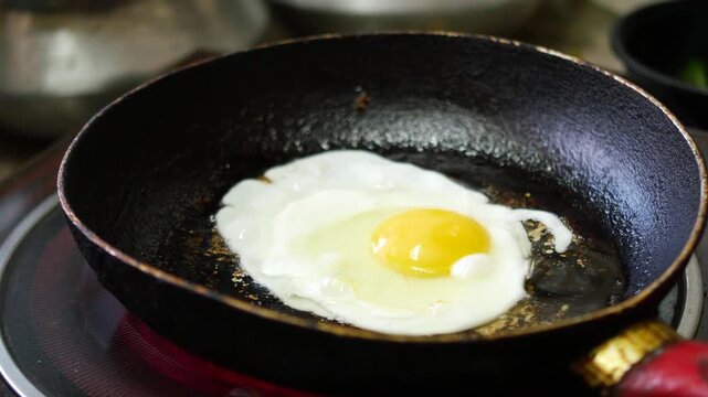 A single egg cooking in a hot pan over a stove top burner, showcasing the vibrant yellow yolk and bubbling white as it cooks, capturing the sizzle and steam of a breakfast favorite