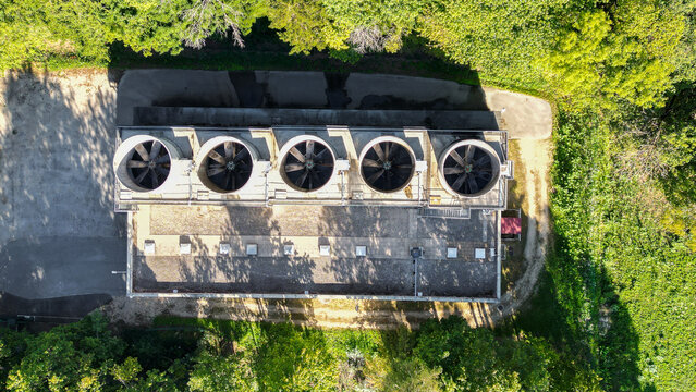 Aerial view of a cooling unit with five large industrial fans on a flat roof surrounded by trees at the European Center for Nuclear Research in Echenevex, Auvergne-Rhone-Alpes, France.