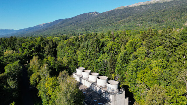 Aerial view of the cooling towers at the European Center for Nuclear Research CERN facility surrounded by dense forest and mountains in Echenevex, Auvergne-Rhone-Alpes, France.