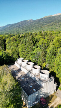 Aerial view of the cooling towers at the European Center for Nuclear Research CERN facility surrounded by dense forest and mountains in Echenevex, Auvergne-Rhone-Alpes, France.