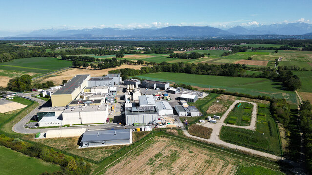 Aerial view of the European Center for Nuclear Research CERN facilities surrounded by green fields and rural landscape in Cessy, Auvergne-Rhone-Alpes, France.