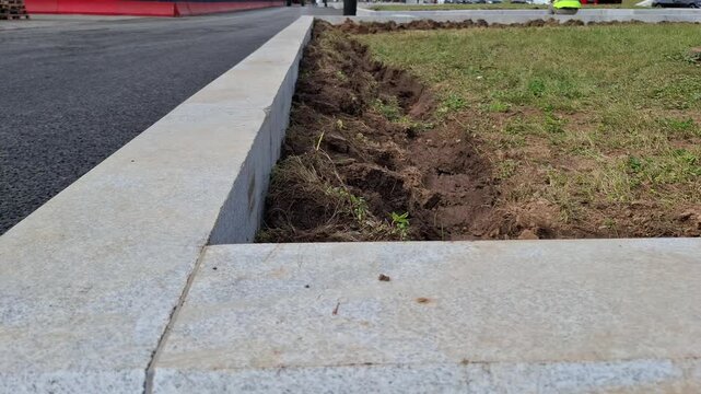 Close up view of installed grey granite curbs next to asphalt and dug soil. stone curb installation, road construction site, street renewal project.