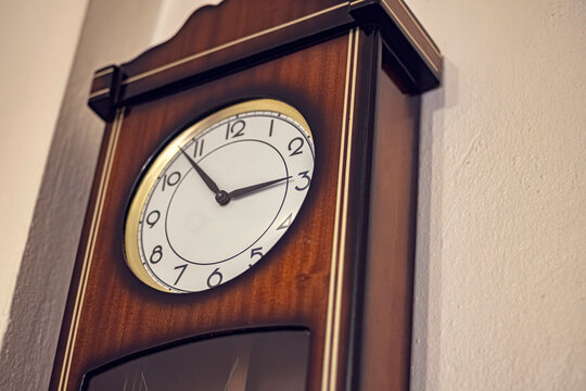 Vintage wooden pendulum wall clock. Pendulum clock detail with gold bezel mounted on a white wall. Use for home decor, antique, nostalgia, and time management themed projects.