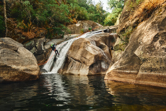 Canyoning participant rappelling down a rushing waterfall with safety ropes