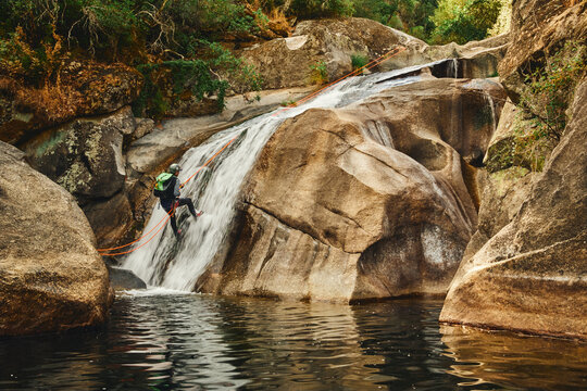 Canyoning adventurer rappelling down a steep waterfall into a dark pool
