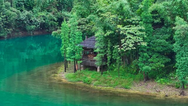 Wooden hut on lush green bank beside emerald river in dense forest