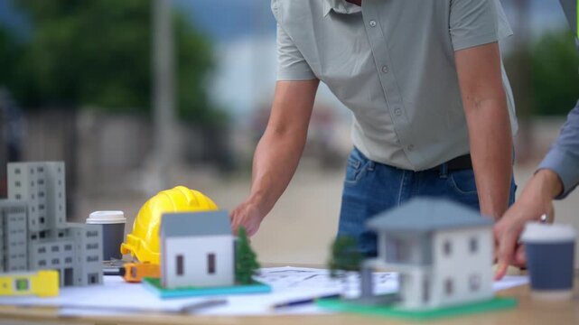 Architect pointing at a house model during a construction project meeting with an engineer on site