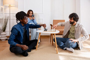 Fototapeta premium Diverse friends playing chess on floor enjoying leisure time