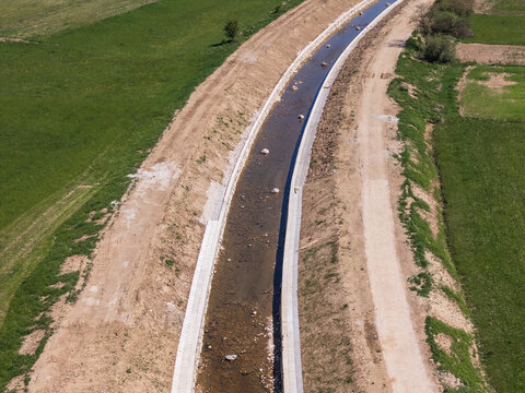 Aerial view of a river restoration project with flood embankment and channel widening taking place near green fields and a dirt path.