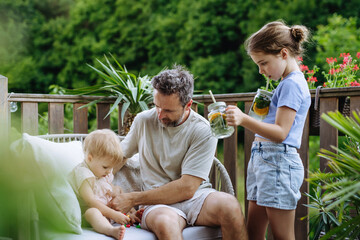 Father enjoying summer drinks with his daughters on outdoor terrace.
